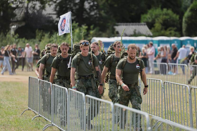 A group of soldiers with a flag  walking in between some fences.