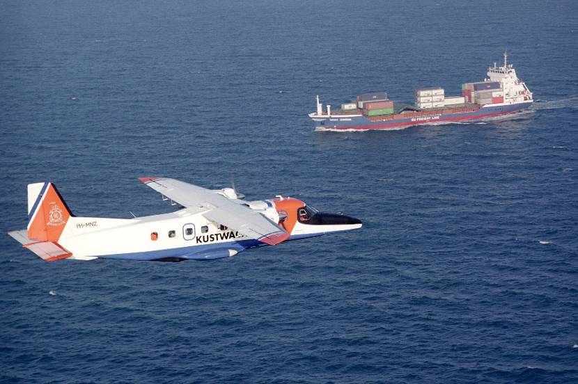 A Dornier 228-212 Marine Patrol over the sea, container ship in the background.