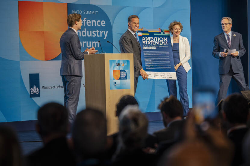 A man and woman are holding a cardboard sign on stage. Two men are watching them from the left and right.