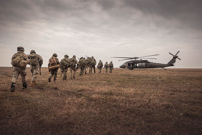 Bepakte landmachtmilitairen lopen naar gereedstaande helikopter.