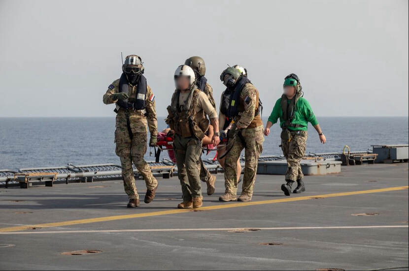 Militairen dragen brancard mt gewonde op achterdek marineschip.
